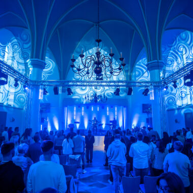 Mitglieder der Gemeinde Neues Leben Kirche in Aachen arbeiten an der Steuerung von Licht und Ton während eines Gottesdienstes. Sie konzentrieren sich darauf, eine einladende und inspirierende Atmosphäre zu schaffen.